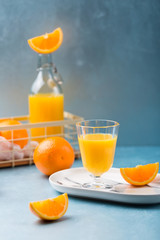 Glass of fresh orange juice with orange slices on white plate, blue background, cold summer refreshing nutritional beverage, blue orange color contrast, vitamin C healthy drink, copy space