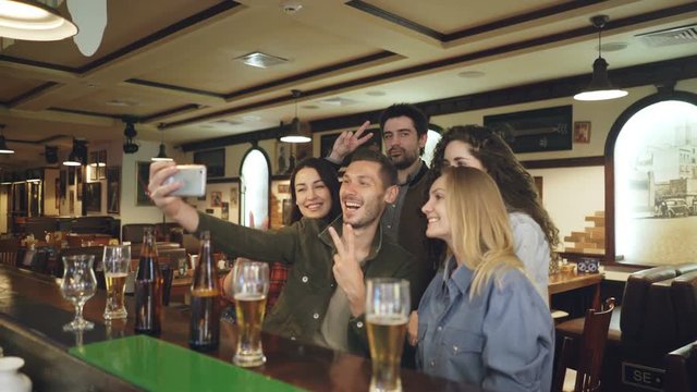 Group of friends are taking selfie via smartphone in nice pub. Beautiful people in casual clothes are posing and having fun. Friendly relaxing atmosphere, happiness concept.