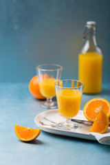 Glass of fresh orange juice with orange slices on white plate, blue background, cold summer refreshing nutritional beverage, blue orange color contrast, vitamin C healthy drink, copy space