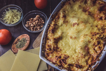 lasagne layered served on a wooden board with fresh tomatoes alongside