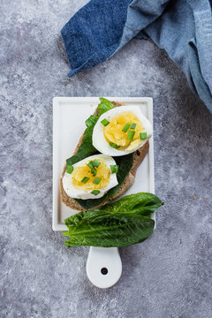 Bread sandwich with spinach and boiled eggs on ceramic plate on gray table background, top view. Healthy Food Diet Snack Concept