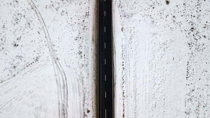 Top view from the air on the winter road in the field on which cars are going