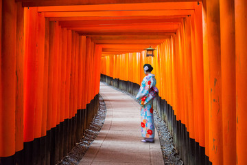 Fototapeta premium Kobieta w tradycyjnej kimonowej pozyci przy tunelem torii bramy, Japonia