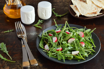 Salad of fresh vegetables - arugula, radish in black plate with flat bread tortilla. Healthy food.