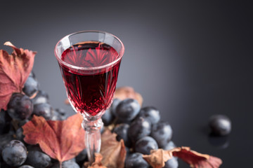 Crystal glass of red wine and grapes with dried vine leaves.