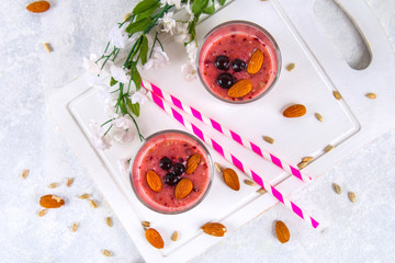 Blueberry smoothies of berries, banana and almonds in glasses with cocktail tubes on a white wooden board.