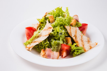 salad with bacon, tomatoes and croutons on a white plate (close)