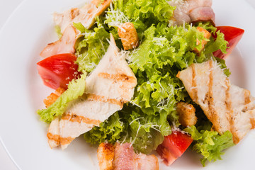 salad with bacon, tomatoes and croutons on a white plate (close)