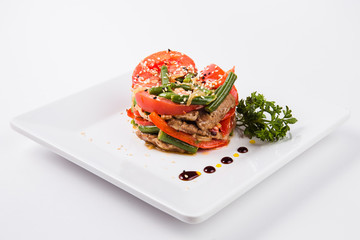 meat salad, tomato decoration on a white plate on a light background