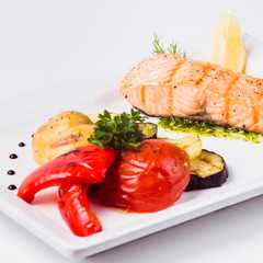 Healthy food, red fish, vegetables, herbs, lemon on a white plate and a white background