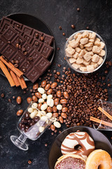 Spilled glasses with coffee beans and peanuts in chocolate on a dark wooden background in studio photo next to other candies