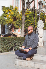 Obraz premium Bearded man with shaved head relaxing by sitting and reading a book in Plaza del Triunfo (Seville, Spain)