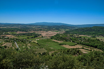 Fototapeta na wymiar Panoramic view of the fields and hills of Provence near Gordes, under sunny blue sky. Located in the Vaucluse department, Provence region, in southeastern France