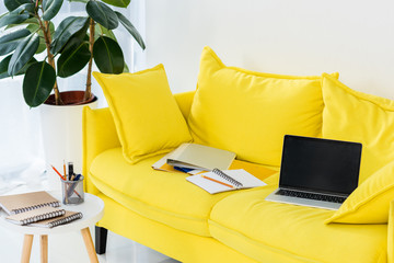 close up view of laptop, notebooks and folders on yellow sofa at home office