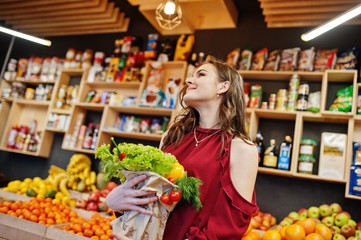 Girl in red holding different vegetables on fruits store.