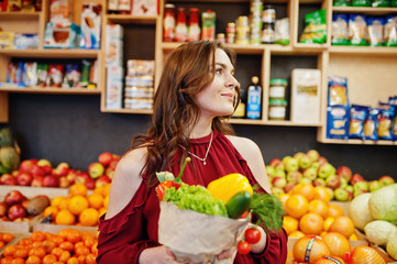 Girl in red holding different vegetables on fruits store.