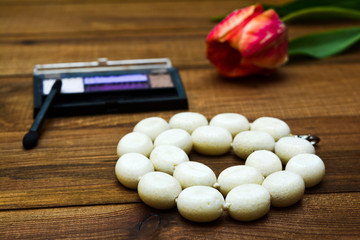 Beads from corals on a wooden background, next to a flower of a tulip and cosmetics.