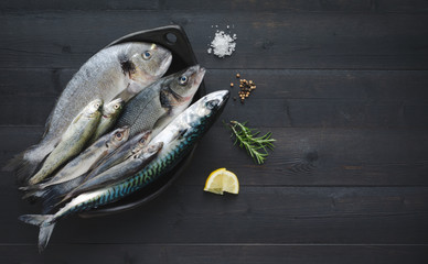 Fresh fish in black bowl on wooden background. Top view.