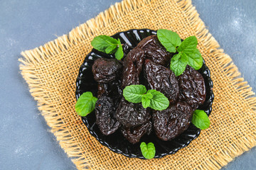 Prunes and fresh mint leaves in a bowl on a concrete table.