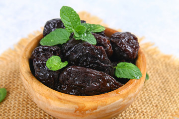 Prunes and fresh mint leaves in a bowl on a concrete table.