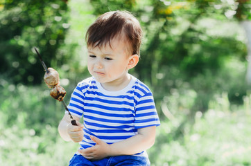 A child eats a kebab on a skewer, in a Park or forest nature green background of trees and grass