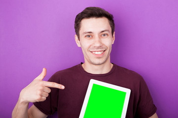 Smiling man pointing with his finger to a digital tablet screen that is green. Perfect for inserting your composit here. Purple background