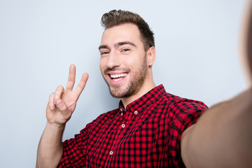 Close up photo of cheerful positive friendly cool attractive handsome stylish guy showing v-sign and taking self portrait, isolated on gray background