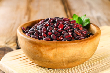 Red raw beans with greens on a wooden table.