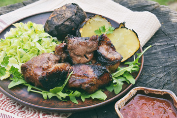 Shashlik with baked potatoes and cabbage salad on clay plate. Marinated meat cooked over charcoal on barbecue grill. Shish kebab. Free space for text.