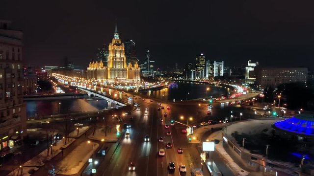The illuminated Hotel "Ukraine" surrounded by river Moskva. Intensive traffic on the city streets. Cityscape and the night lights on the New Arbat street and Kutuzovski avenue.