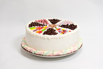 Delicious multicolored child cake decorated with candy and confetti. Side view, isolated on white background.