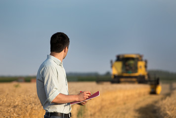 Engineer with notebook and combine harvester in field