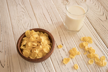 Delicious corn flakes in a clay bowl with a glass of milk. Rustic wood background. Healthy crispy snack for Breakfast.