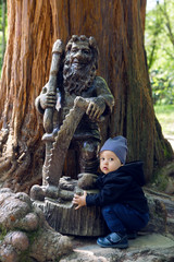 child sits with a tree and a wooden sculpture
