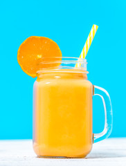 Orange smoothie with tropical fruit or cocktail with fruits blended with milk, cold summer drink on blue background