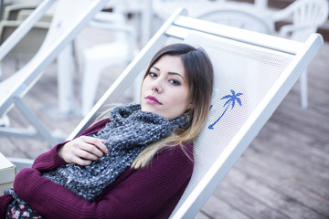 Giovane ragazza bionda è seduta in uno sdraio in un chiosco al mare in una giornata invernale.