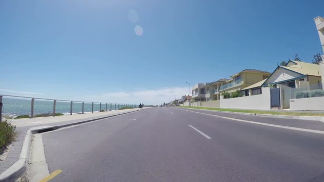 Vehicle POV, driving along The Esplanade, Henley Beach, South Australia, with views of ocean and beach, and homes overlooking the sea.