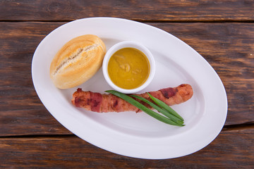Sausage on a white plate and a dark wooden background with bread and sauce