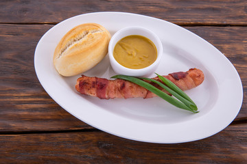 Sausage on a white plate and a dark wooden background, with onions, sauce and bread