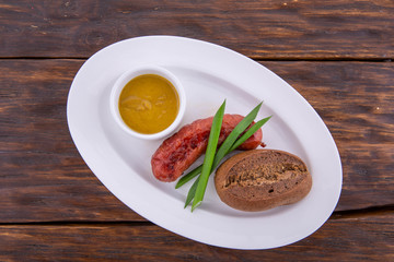 The sausage fried on coals is served on a white plate and a dark wooden background
