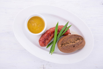 Fried beef sausage on a white plate and a white wooden background with onions, sauce and bread