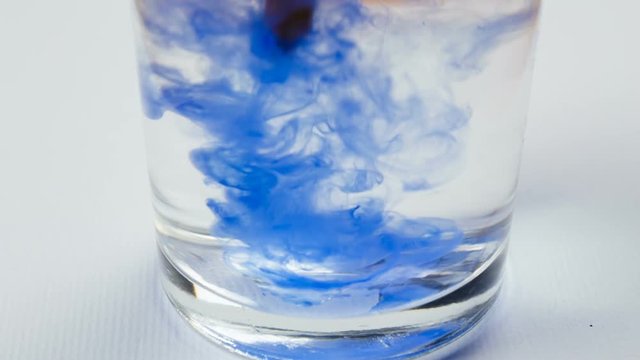 blue watercolor paint drops dissolve on water in glass