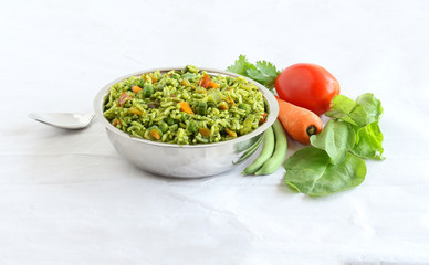 Palak rice, biryani or pilaf, which is made from spinach and vegetables like tomato, carrot and long green beans, is an Indian vegetarian healthy food, in a steel bowl.