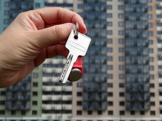 House purchase. Real estate agent holding house key on background of new buildings. Moving home or renting property