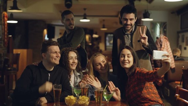 Happy young people in casual clothes are taking selfie in bar. They are posing, making silly faces, laughing and gesturing. Funny photos for good memories concept.