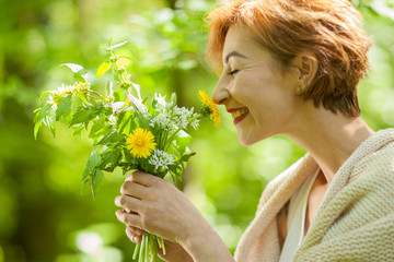 Beautiful woman holding wild herbs, smelling and smiling, in the forest, can be used as background - 203369607