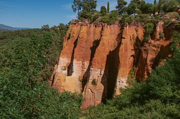 View of ocher land cliffs under a sunny blue sky, in a park near the village of Roussillon. Located...