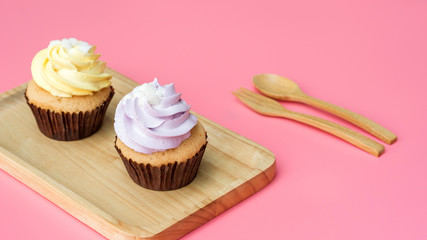 Cupcake on a wooden plate and pink background.