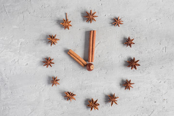 Cinnamon sticks star anise laid Out in the form of arrows and clock face on a gray concrete background