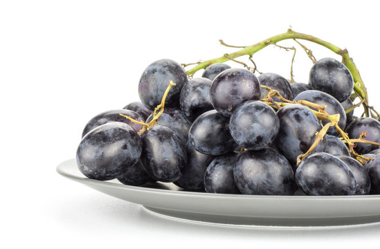 Black purple grape cluster (autumn royal variety) on a grey ceramic plate isolated on white background.